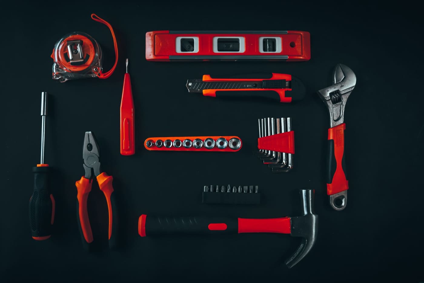 Flat lay of a tape measure, level, screwdrivers, pliers, wrench and hammer on a dark surface