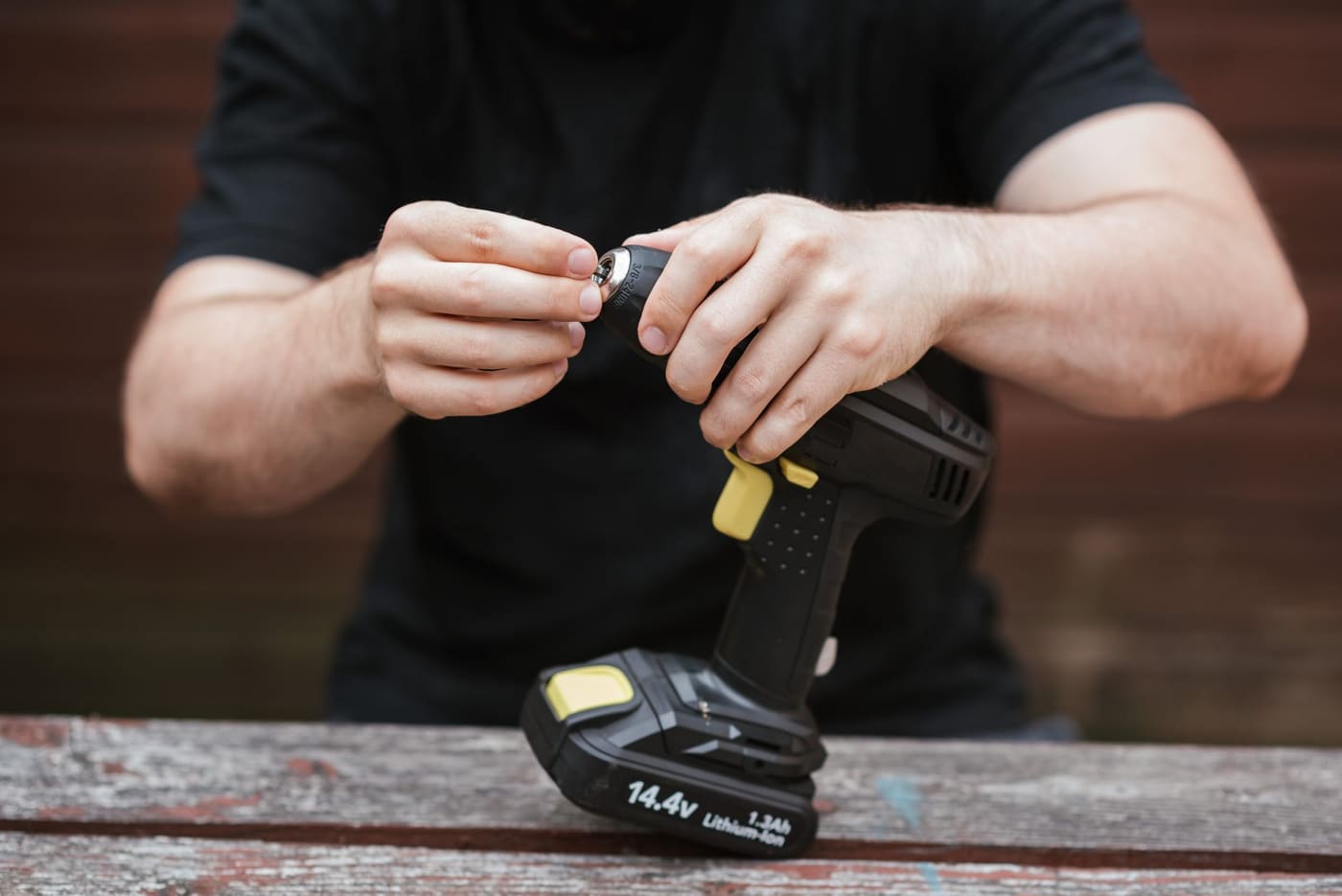 A person clicking a battery pack into the handle of a cordless drill on a wooden table