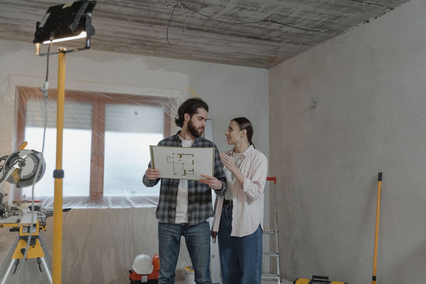 A man and a woman looking over a printed plan in a partly renovated room with work lights