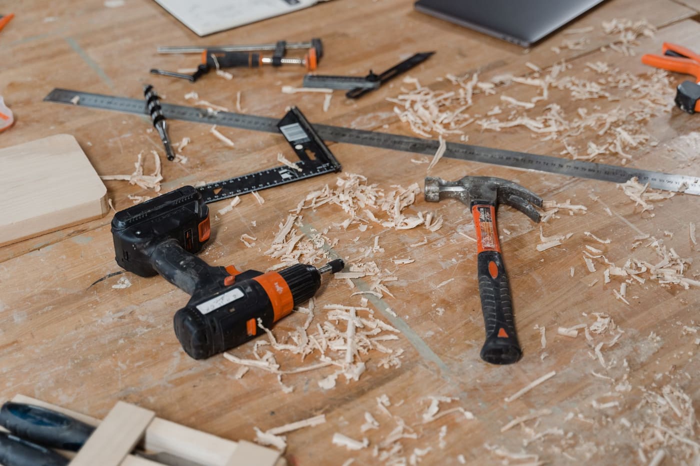 A cordless drill and a claw hammer on a wooden workbench with wood shavings