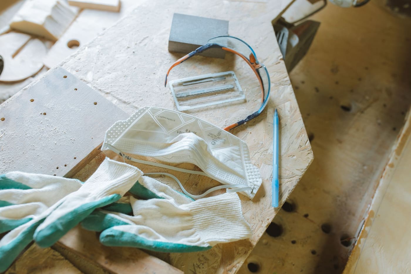 Work gloves, a dust mask and safety goggles lying on a wooden work table