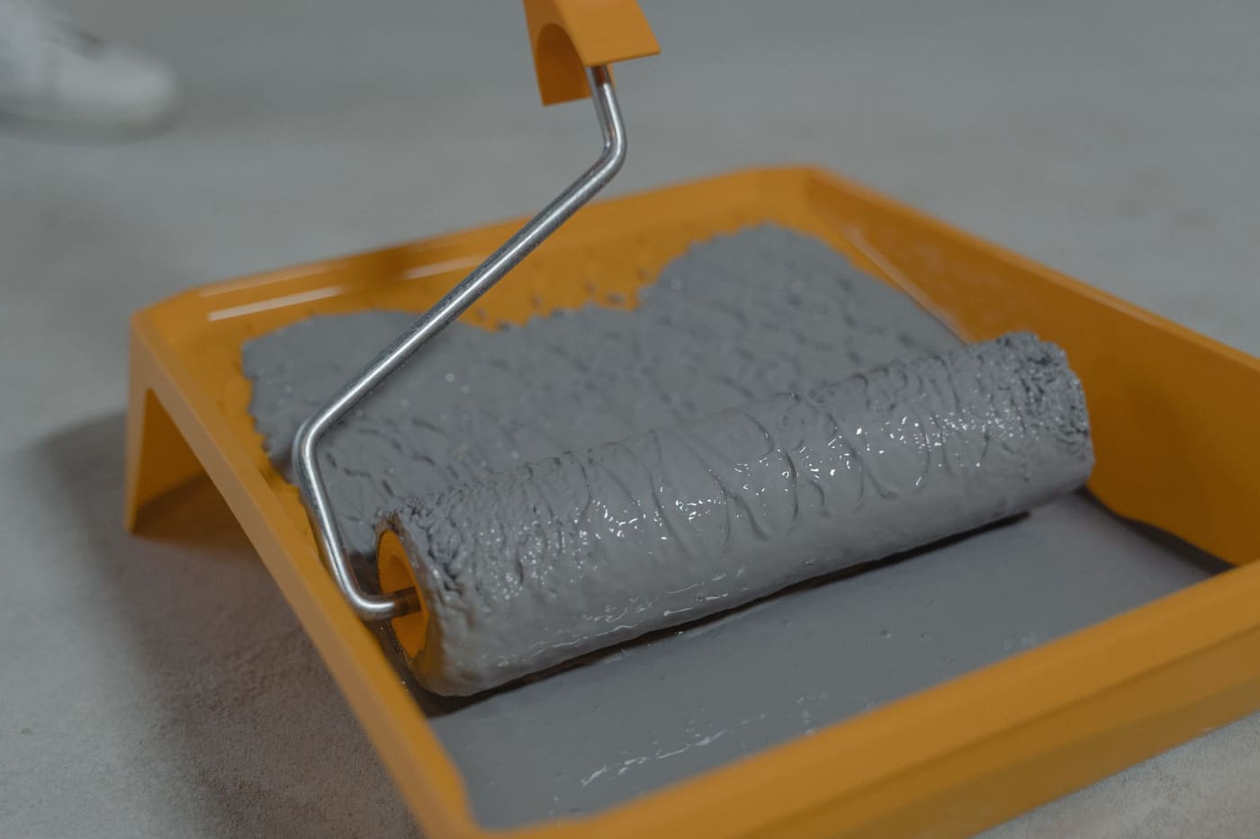 A grey paint roller loaded with paint in a yellow roller tray