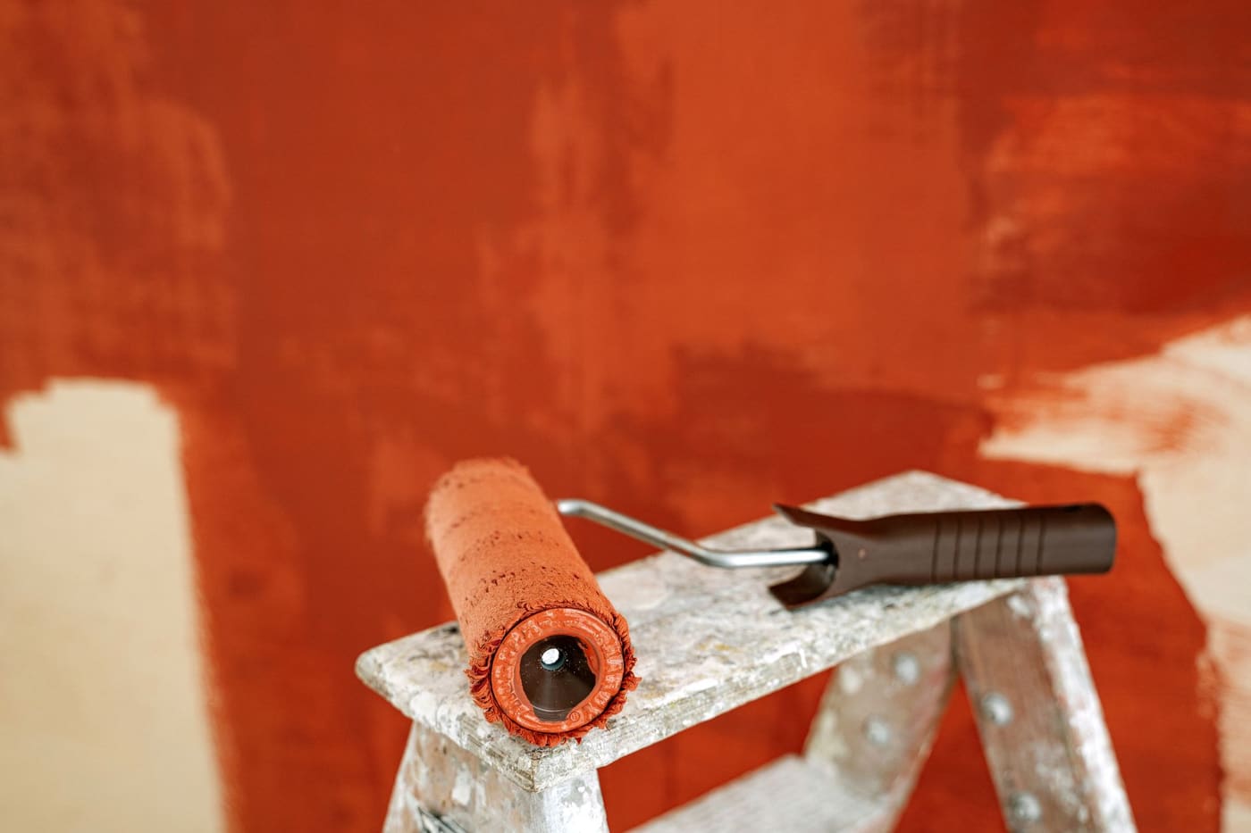 A paint roller resting on a stepladder in front of a partly painted wall