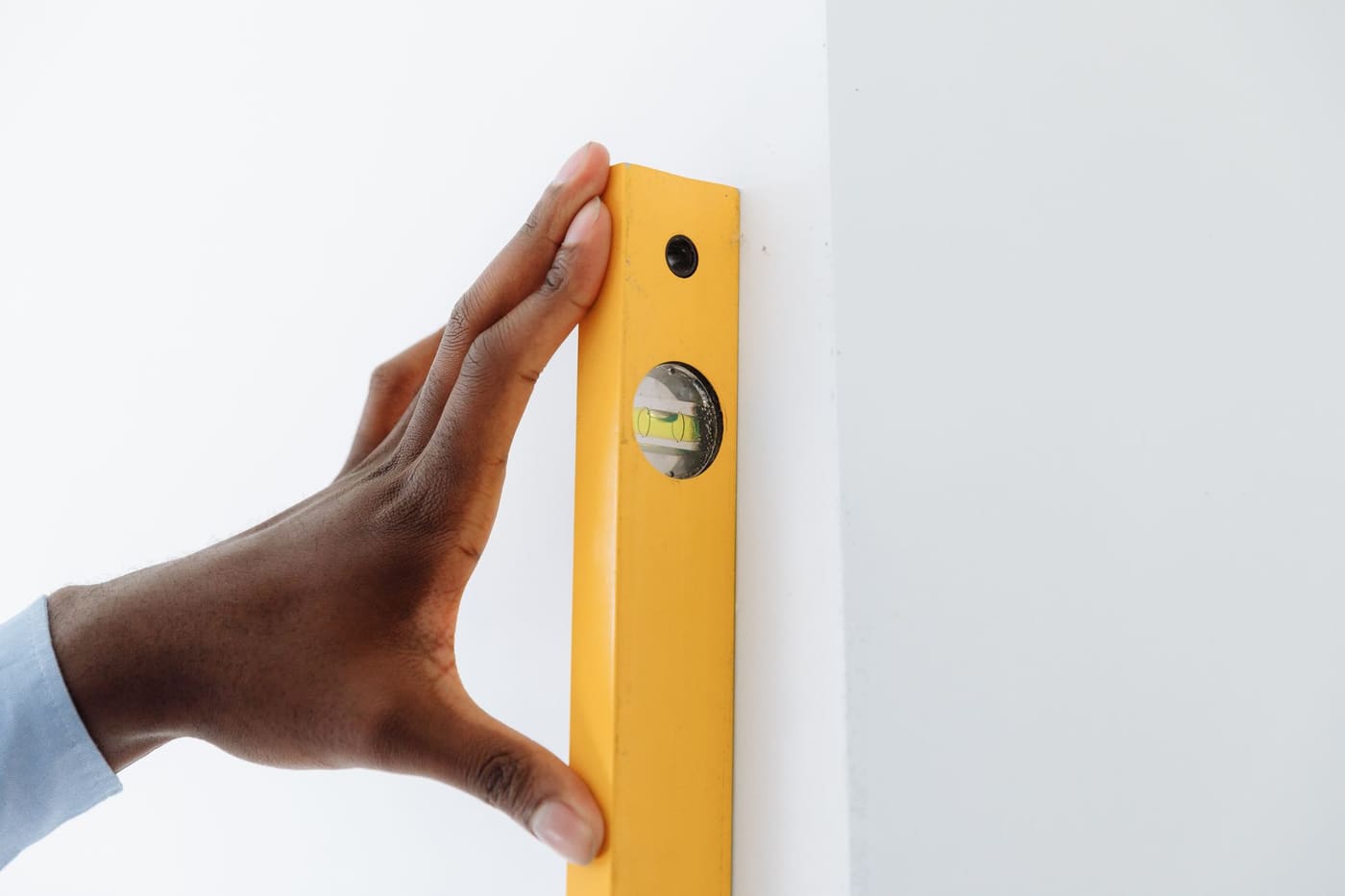 A hand pressing a yellow level against a white wall to check that it is vertical